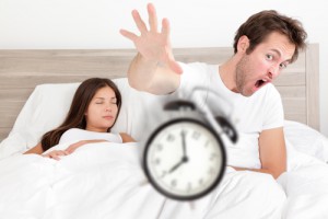Wake up - couple waking up early throwing alarm clock. Funny bed concept with young interracial couple waking up late. Man throwing alarm clock, and woman sleeping. Asian female, Caucasian male models