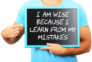 Man holding blackboard in hands and pointing the word I AM WISE BECAUSE I LEARN FROM MY MISTAKES