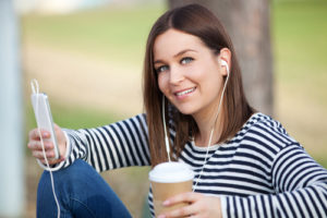 Beautiful young woman listening to music and having takeaway coffee outdoors