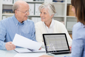 Elderly couple in a meeting with an adviser discussing a document as she watches across the desk in her office