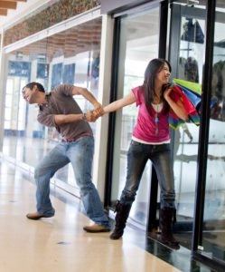Man keeping a woman from entering a store and begging her to stop shopping