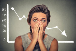 Shocked scared woman with financial market chart graphic going down on grey office wall background. Poor economy concept. Face expression, emotion, reaction