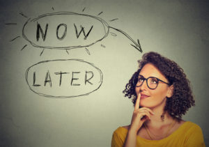 Now or later. Woman thinking looking up isolated on grey wall background. Human face expression