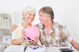 Portrait Of Smiling Senior Couple Saving Money In The Pink Piggybank